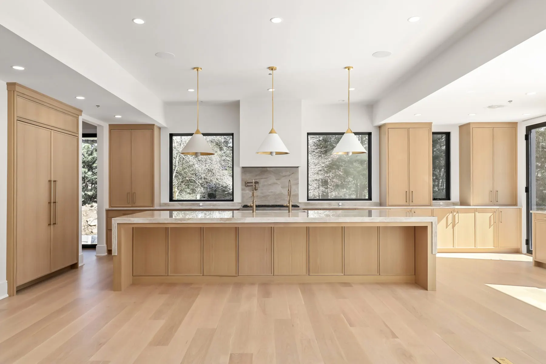 A white oak kitchen with a stone waterfall island and brass pendant lights